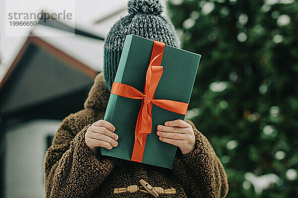 Junge versteckt Gesicht mit Weihnachtsgeschenk