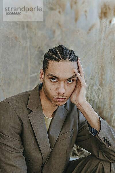 Young businessman with cornrow hairstyle sitting in garden