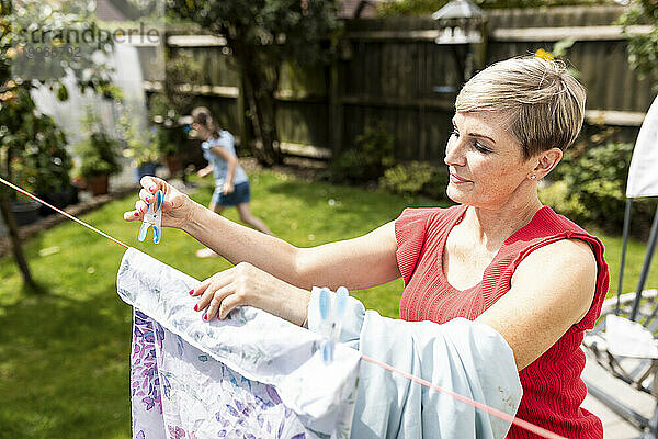 Mother drying clothes rope with daughter playing in back yard