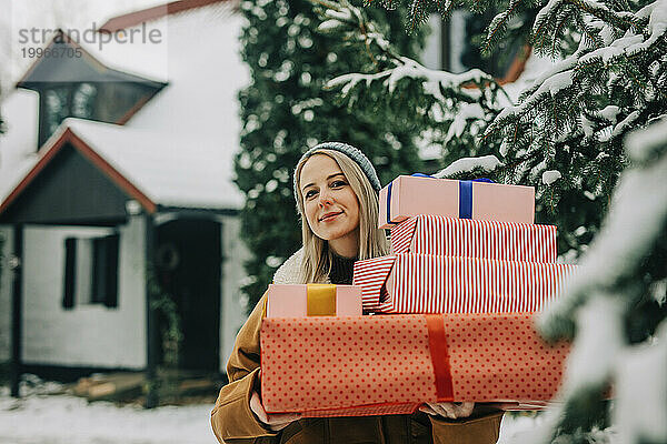 Lächelnde Frau hält Weihnachtsgeschenke neben Baum