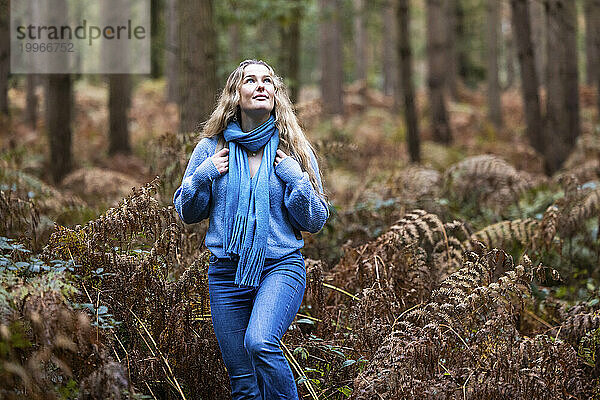 Lächelnde blonde Frau  die in der Nähe von Pflanzen im Wald von Cannock Chase spaziert