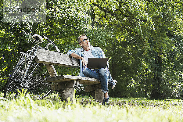 Nachdenklicher älterer Mann mit Laptop sitzt auf Bank