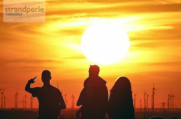 Menschen am Berliner Drachenberg zum Sonnenuntergang. Im Hintergrund ist ein Windpark bei Nauen in Brandenburg zu sehen  23.08.2022