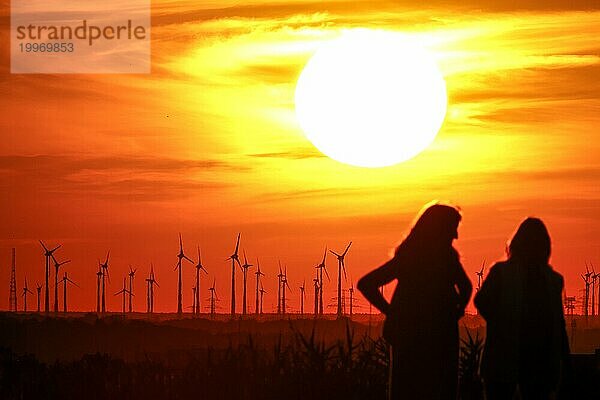 Menschen am Berliner Drachenberg zum Sonnenuntergang. Im Hintergrund ist ein Windpark bei Nauen in Brandenburg zu sehen  23.08.2022