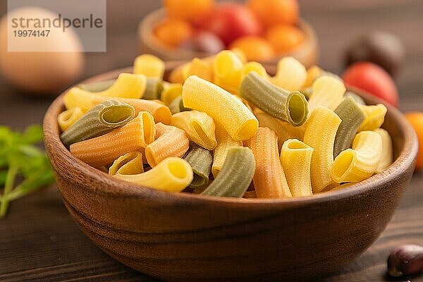 Rigatoni farbige rohe Nudeln mit Tomaten  Eiern  Gewürzen  Kräutern auf braunem Holzhintergrund. Seitenansicht  Nahaufnahme  selektiver Fokus