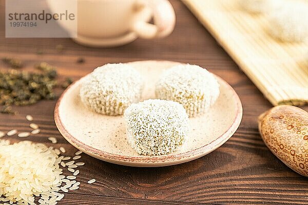 Japanischer Reis süße Brötchen Mochi gefüllt mit Pandan und Kokosnuss Marmelade und Tasse grüner Tee auf braunem Holz Hintergrund. Seitenansicht  Nahaufnahme  selektiver Fokus