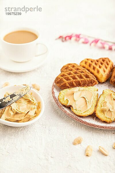 Hausgemachte Waffel mit Erdnussbutter und Tasse Kaffee auf einem grauen Betonhintergrund. Seitenansicht  Nahaufnahme  selektiver Fokus