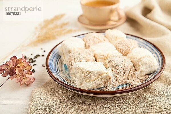 Traditionelle arabische Süßigkeiten Pishmanie und eine Tasse grüner Tee auf weißem hölzernem Hintergrund und Leinenstoff. Seitenansicht  Nahaufnahme  selektiver Fokus