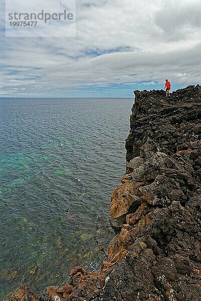 Eine mutige Person steht am Rande einer hohen vulkanischen Klippe über dem Meer  Lavafelsen Küstenwanderweg Ponta da Iiha  Calhau  Westküste  Pico  Azoren