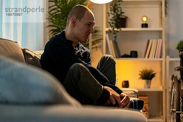 Behinderter Mann sitzt allein auf dem Sofa mit traurigem Gesichtsausdruck in der Nacht