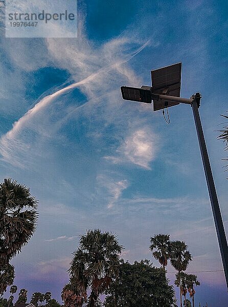 Die Silhouette einer solarbetriebenen Straßenlaterne am Abendhimmel mit Wolken und Palmen  nachhaltiges Leben