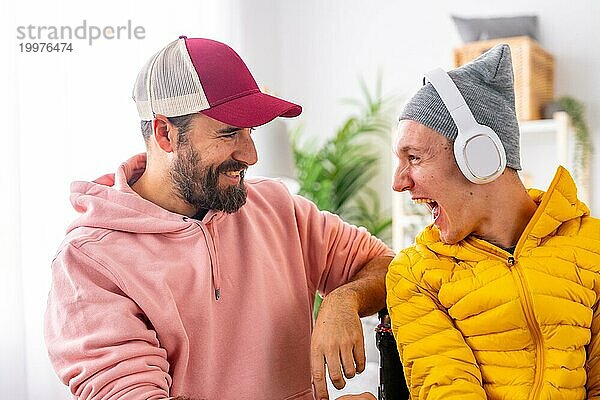 Aufgeregter behinderter Mann  der zu Hause mit einem Freund über Kopfhörer Musik hört