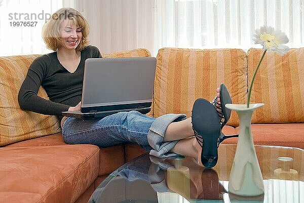 Junge Frau mit laptop sitzt auf einer Couch