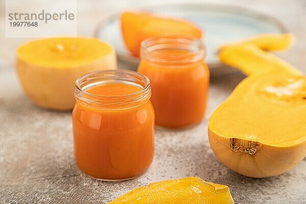 Baby Püree mit Früchten mischen  Kürbis  Kaki  Mango Säuglingsnahrung in Glasgefäß auf braunem Beton Hintergrund. Seitenansicht  Nahaufnahme  selektiver Fokus  künstliche Ernährung Konzept