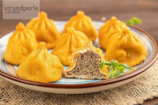 Gebratene Manti Knödel mit Pfeffer  Basilikum auf braunem Holzhintergrund und Leinenstoff. Seitenansicht  Nahaufnahme  selektiver Fokus