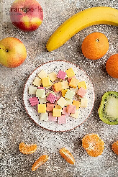 Verschiedene Fruchtgelee Kaubonbons auf Teller auf braunem Betonhintergrund. Apfel  Banane  Mandarine  Draufsicht  Flachlage  Nahaufnahme
