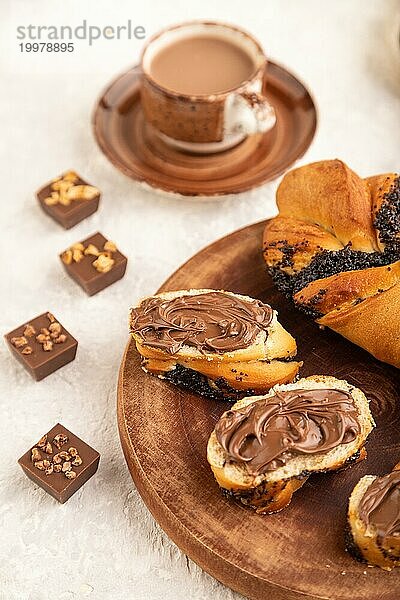 Hausgemachtes süßes Brötchen mit Schokoladencreme und Tasse Kaffee auf grauem Betonhintergrund und Leinenstoff. Seitenansicht  Nahaufnahme  selektiver Fokus