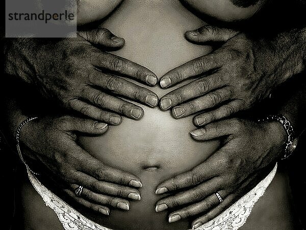 Junge Frau mit 4 Händen auf dem Babybauch