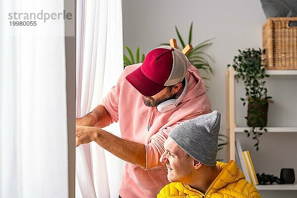 Ein neugieriger behinderter Mann und sein Freund schauen durch das Fenster in einem warmen Wohnzimmer