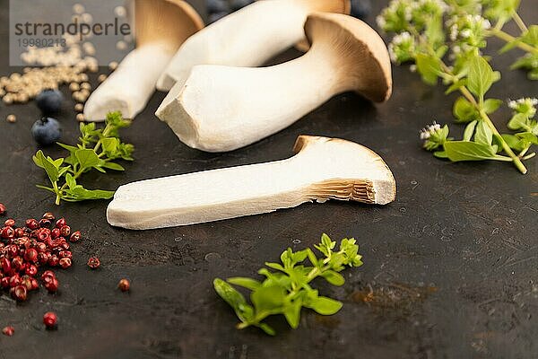 Braune Kräuter Seitlinge (Pleurotus eryngii) auf schwarzem Betonhintergrund mit Heidelbeeren  Kräutern und Gewürzen. Seitenansicht  selektiver Fokus