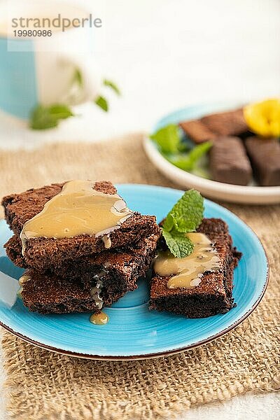 Schokoladen Brownie mit Karamellsauce und einer Tasse Kaffee auf grauem Betonhintergrund und Leinenstoff. Seitenansicht  Nahaufnahme  selektiver Fokus