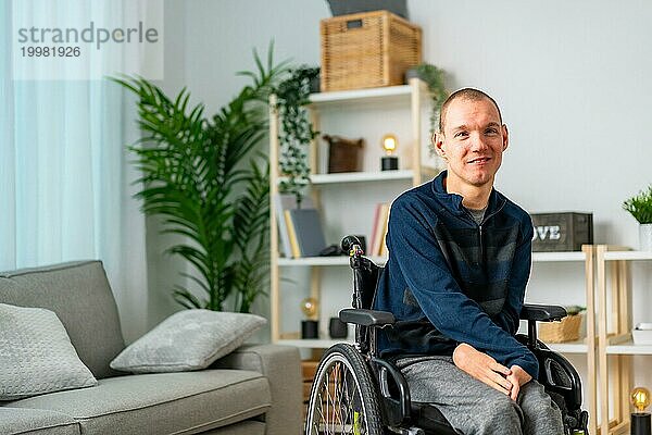 Porträt eines fröhlichen behinderten Mannes im Rollstuhl  der in die Kamera lächelt und sich zu Hause entspannt