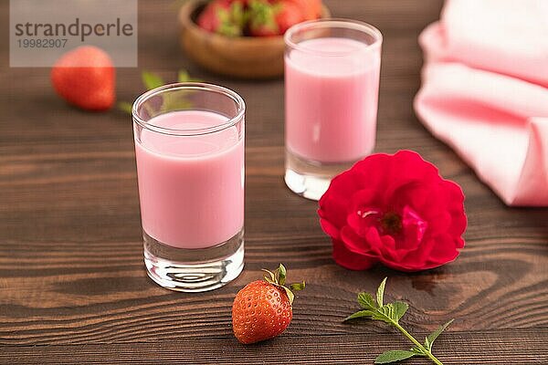 Süßer Erdbeerlikör in einem Glas auf einem braunen Holzhintergrund und rosa Stoff. Seitenansicht  Nahaufnahme  selektiver Fokus