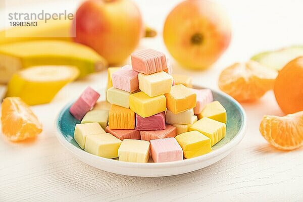 Verschiedene Fruchtgelee Kaubonbons auf einem Teller auf weißem Holzhintergrund. Apfel  Banane  Mandarine  Kiwi  Seitenansicht  Nahaufnahme  selektiver Fokus