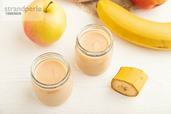 Baby Püree mit Früchten mischen  Apfel  Banane Säuglingsnahrung in Glasgefäß auf weißem Holz Hintergrund. Seitenansicht  Nahaufnahme  selektiver Fokus  künstliche Ernährung Konzept