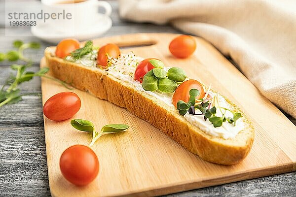 Langes Weißbrot Sandwich mit Frischkäse  Tomaten und Mikrogrün auf grauem Holzhintergrund und Leinenstoff. Seitenansicht  Nahaufnahme  selektiver Fokus