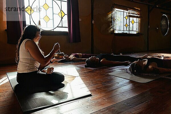 Frau im Lotussitz leitet eine Meditationssitzung. Entspannender Moment nach einer Yoga Gruppenstunde. Leuchtender Kontrast