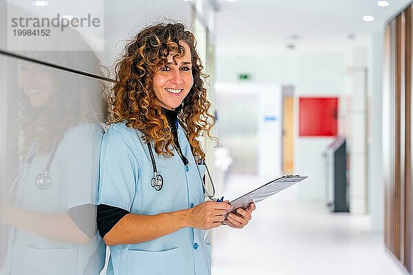 Glückliche Krankenschwester schaut in die Kamera und lächelt bei der Arbeit im Krankenhaus