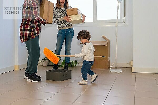 Ausgeschnittenes Foto eines kleinen Mädchens  das mit einem Besen spielt  während Erwachsene ein Haus umstellen