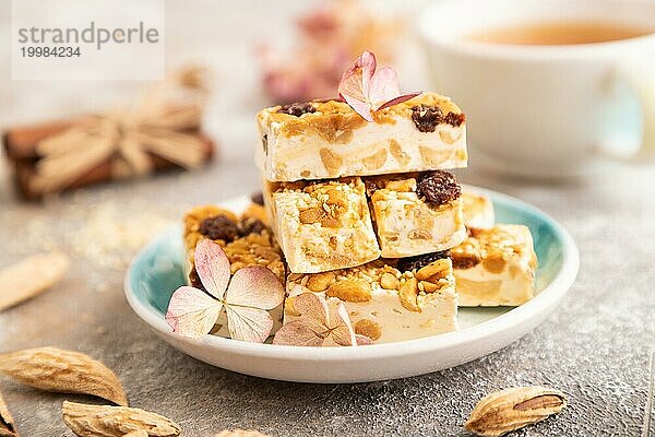 Traditionelle Süßigkeiten Nougat mit Nüssen und Sesam mit Tasse grünem Tee auf braunem Beton Hintergrund. Seitenansicht  Nahaufnahme  selektiver Fokus