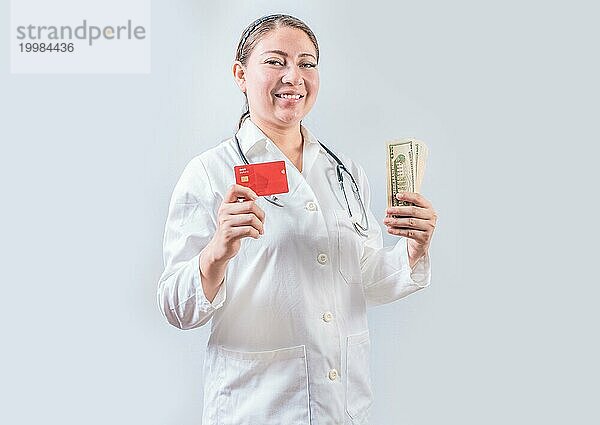 Schöne und lächelnde Ärztin hält Geld und Kreditkarten. Glückliche Ärztin hält Kreditkarte und Geld isoliert