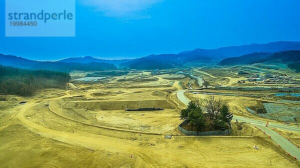 Luftaufnahme einer Baustelle mit einer kleinen Baumgruppe  die zum Schutz eingezäunt ist  und sanften Hügeln unter blauem Himmel im Hintergrund  Südkorea  Südkorea  Asien