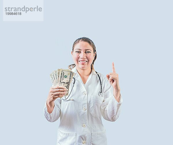 Lächelnde Ärztin hält Geld und zeigt nach oben isoliert. Glückliche junge Ärztin zeigt Geld und zeigt auf Promo up