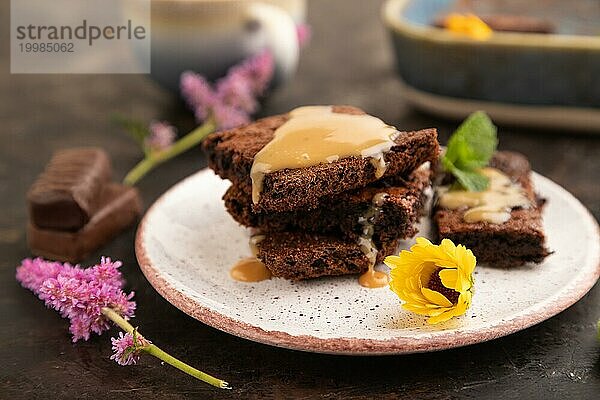 Schokolade Brownie mit Karamell Sauce mit einer Tasse Kaffee auf schwarzem Beton Hintergrund. Seitenansicht  Nahaufnahme  selektiver Fokus