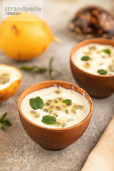 Joghurt mit Granadilla und Minze in Tonschale auf braunem Betonhintergrund und orangefarbenem Leinentextil. Seitenansicht  Nahaufnahme  selektiver Fokus