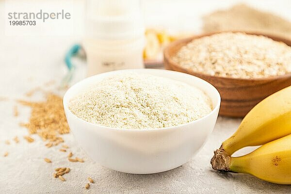 Milchpulver und Haferflocken  Bananen Babynahrungsmischung  Säuglingsnahrung  Schnuller  Flasche  Löffel auf grauem Betonhintergrund. Seitenansicht  Nahaufnahme  selektiver Fokus  Konzept der künstlichen Ernährung