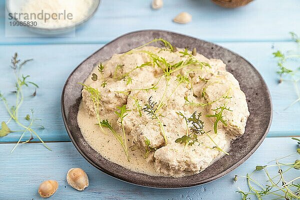 Geschmorte Hühnerfilets mit Kokosmilchsauce und Mizunakraut Mikrogrün auf blauem Holzhintergrund. Seitenansicht  Nahaufnahme  selektiver Fokus