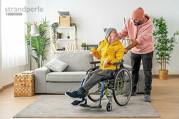 Glücklicher behinderter Mann mit einem Freund  der den Rollstuhl zu Hause hält