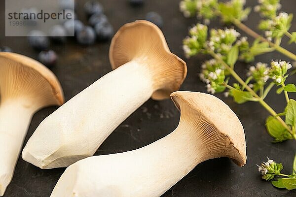 Braune Kräuter Seitlinge (Pleurotus eryngii) auf schwarzem Betonhintergrund mit Heidelbeeren  Kräutern und Gewürzen. Seitenansicht  selektiver Fokus