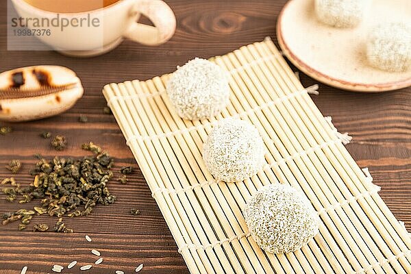 Japanischer Reis süße Brötchen Mochi gefüllt mit Pandan und Kokosnuss Marmelade und Tasse grüner Tee auf braunem Holz Hintergrund. Seitenansicht  Nahaufnahme  selektiver Fokus