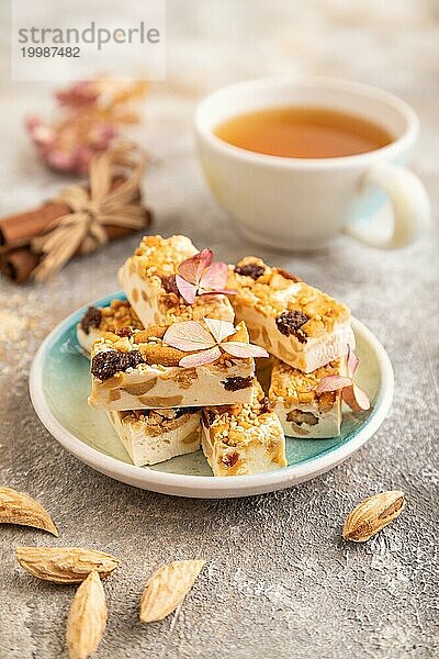 Traditionelle Süßigkeiten Nougat mit Nüssen und Sesam mit Tasse grünem Tee auf braunem Beton Hintergrund. Seitenansicht  Nahaufnahme  selektiver Fokus