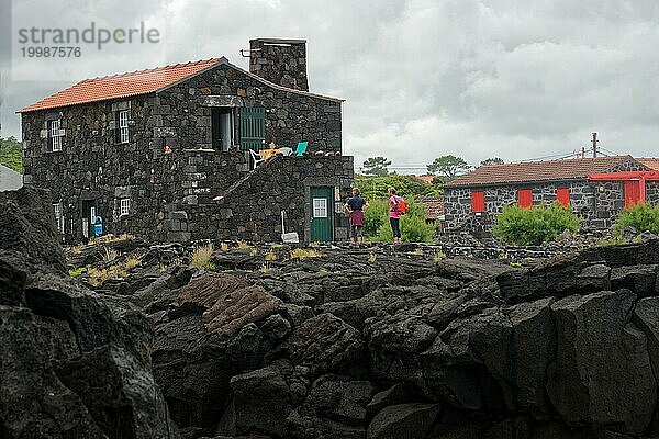 Menschen stehen neben einem Steinhaus auf Lavagestein unter einem bedeckten Himmel  Nordküste  Santa Luzia  Pico  Azoren  Portugal  Europa