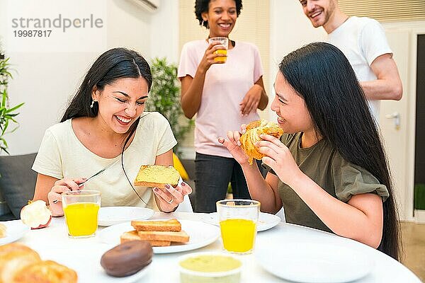 Eine Gruppe verschiedener multiethnischer Freunde lacht beim Frühstück zu Hause