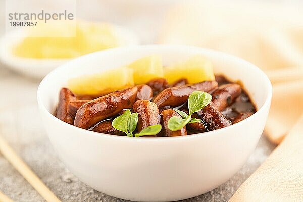 Tteokbokki oder Topokki  gebratener Reiskuchen am Stiel  beliebtes koreanisches Straßenessen mit würziger Jjajang Sauce und Ananas auf grauem Betonhintergrund und orangefarbenem Textil. Seitenansicht  Nahaufnahme  selektiver Fokus