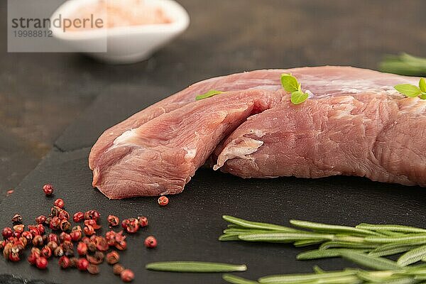 Rohes Schweinefleisch mit Kräutern und Gewürzen auf Schiefer Schneidebrett auf schwarzem Beton Hintergrund. Seitenansicht  Nahaufnahme  selektiver Fokus