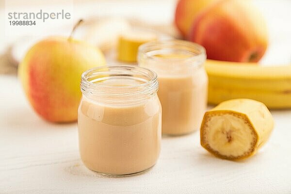 Baby Püree mit Früchten mischen  Apfel  Banane Säuglingsnahrung in Glasgefäß auf weißem Holz Hintergrund. Seitenansicht  Nahaufnahme  selektiver Fokus  künstliche Ernährung Konzept